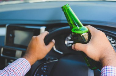Genç adam araba sürerken bira içiyor.