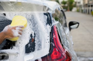 Adam arabayı sünger ve köpükle temizliyor.