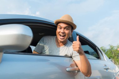 Genç Asyalı adam araba sürerken baş parmağını gösteriyor..