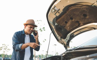 Genç bir Asyalı turist bir araba sürdü ve yolda bozuldu. Kaputa bakmaya geldi ve yardım için tamirciyi çağırdı..