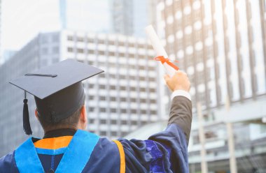 Mutlu mezun. Mezuniyet elbiseli mutlu Asain adam şehir geçmişi üzerine diplomasını elinde tutuyor..