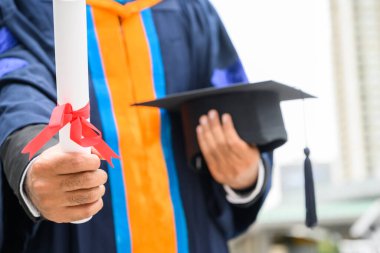 Mutlu mezun. Mezuniyet elbiseli mutlu Asain adam şehir geçmişi üzerine diplomasını elinde tutuyor..