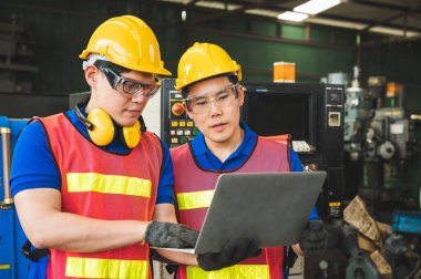 Asyalı endüstriyel işçiler büyük sanayi tesislerinde dizüstü bilgisayarlarla proje çalışmalarını tartışıyorlar.
