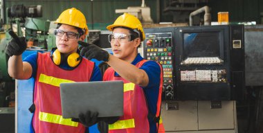 Asyalı endüstriyel işçiler büyük sanayi tesislerinde dizüstü bilgisayarlarla proje çalışmalarını tartışıyorlar.