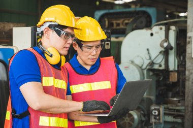 Asyalı endüstriyel işçiler büyük sanayi tesislerinde dizüstü bilgisayarlarla proje çalışmalarını tartışıyorlar.