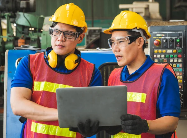 Asian industrial workers are discussing project work in large industrial plants with laptops.