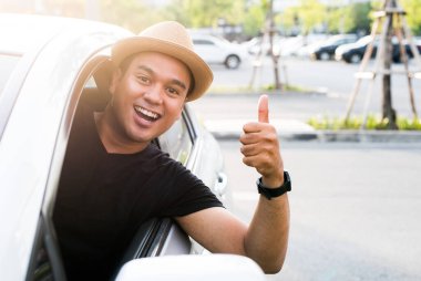 Asyalı genç adam fotokopi alanı olan arabayı sürerken başparmağını kaldırıyor..