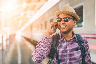 Genç adam tren istasyonunda duruyor ve akıllı telefon kullanıyor.