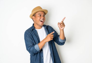 30 yaşındaki mutlu Asyalı adam, şapka takıyor, kot gömlek giyiyor, duruyor, boş bir yeri işaret ediyor..