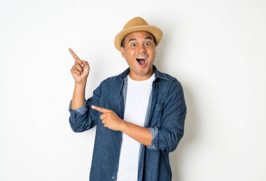 30 yaşındaki mutlu Asyalı adam, şapka takıyor, kot gömlek giyiyor, duruyor, boş bir yeri işaret ediyor..