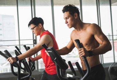 Spor salonunda bir grup insan çapraz antrenör makinesinde egzersiz yapıyor. Genç fitness erkekleri ve kadınlar yeni başlayanlar için kardiyo çalışması yapıyorlar..