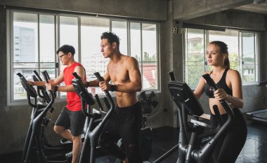 Spor salonunda bir grup insan çapraz antrenör makinesinde egzersiz yapıyor. Genç fitness erkekleri ve kadınlar yeni başlayanlar için kardiyo çalışması yapıyorlar..
