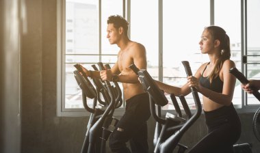 Spor salonunda bir grup insan çapraz antrenör makinesinde egzersiz yapıyor. Genç fitness erkekleri ve kadınlar yeni başlayanlar için kardiyo çalışması yapıyorlar..