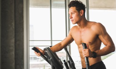 Spor salonundaki genç adam çapraz antrenör makinesinde egzersiz yapıyor. Fitness adamı kardiyo çalışması yapıyor..
