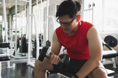 Güçlü kaslı Asyalı adam spor salonunda bisepslerde egzersiz yapıyor. Ağırlık antrenmanı konsepti.