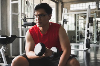 Güçlü kaslı Asyalı adam spor salonunda bisepslerde egzersiz yapıyor. Ağırlık antrenmanı konsepti.