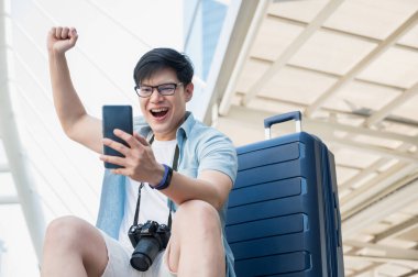 Asyalı gezgin şehir arka planında tramvay çantalı akıllı telefona bakarken mutlu.