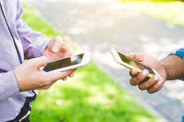 Parkta akıllı telefon kullanan iki işadamı..