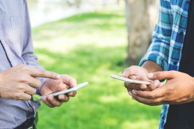 Parkta akıllı telefon kullanan iki işadamı..