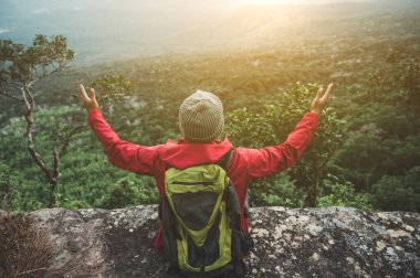 Kırmızı yağmurluk giyen yürüyüşçüler bir sırt çantası taşıyorlar bir uçurumun kenarında oturuyorlar gün batımında dağların güzelliğine bakın, başarı, özgürlük ve macera gösteriyorlar..