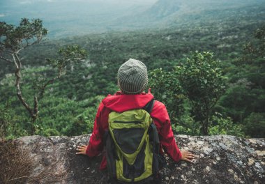 Kırmızı yağmurluk giyen yürüyüşçüler bir sırt çantası taşıyorlar bir uçurumun kenarında oturuyorlar gün batımında dağların güzelliğine bakın, başarı, özgürlük ve macera gösteriyorlar..