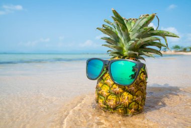 Tropik plaj arka planında güneş gözlüklü ananas. Yaz konsepti