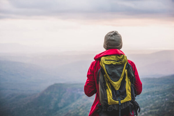 Hikers climbing a red rain jacket carrying a backpack Standing on the edge of a cliff See the beauty of the mountains at sunset, showing success, freedom and adventure.