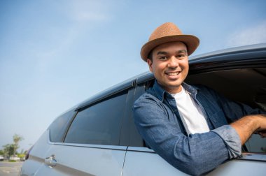 Asyalı bir adam seyahatinin tadını çıkarıyor. Onu mutlu etmek için arabanın camından dışarı uzanıyor..