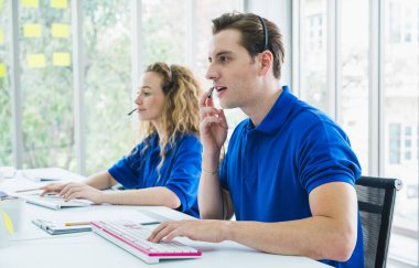 Müşteri destek operatörü. Takım İş ve Teslimat Merkezi ofisinde. Mavi üniformalı bir kulaklıkla çalışıyor..