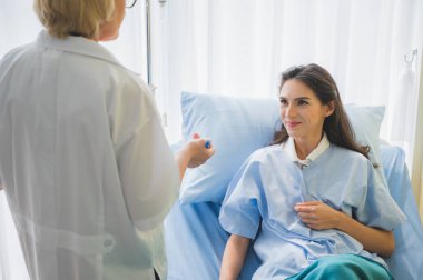 Kıdemli kadın doktor ve hasta yatakta yatarken belirtiler hakkında tartışıp not alıyorlar..