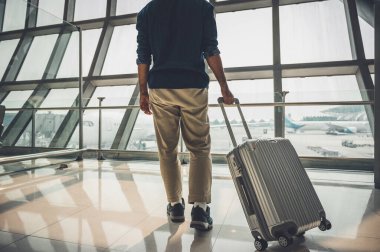Seyahate çıkmaya hazırlanan gri şapkalı bir erkek yolcu. Bir tramvay çantası var. Dünyayı dolaşmak için büyük bir havaalanında duruyor..