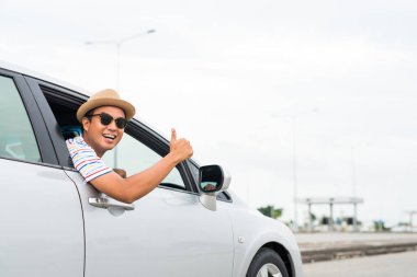 Genç Asyalı adam araba sürerken baş parmağını gösteriyor..