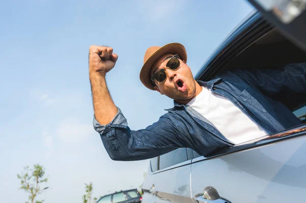 An Asian man is enjoying his trip. He stretches out of the car window to make him look happy.