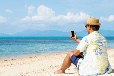 Genç Asyalı sahilde akıllı telefon kullanıyor..