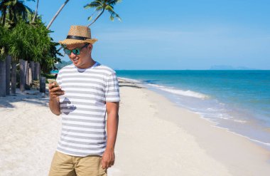 Genç Asyalı sahilde akıllı telefon kullanıyor..