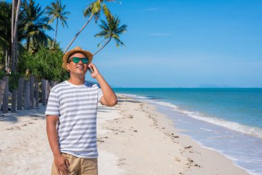 Genç Asyalı sahilde akıllı telefon kullanıyor..