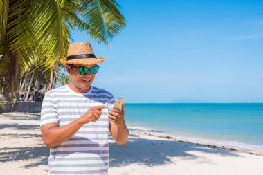 Genç Asyalı sahilde akıllı telefon kullanıyor..