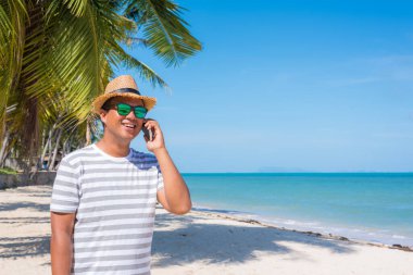 Genç Asyalı sahilde akıllı telefon kullanıyor..