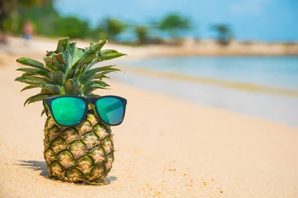 Tropik plaj arka planında güneş gözlüklü ananas. Yaz konsepti
