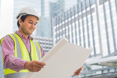 Genç Asyalı mühendis ileriye bakıyor ve inşaat planını tutuyor. İnşaat yöneticisi kavramı.