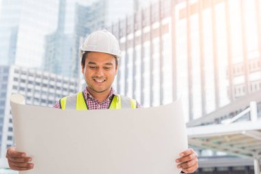 Genç Asyalı mühendis ileriye bakıyor ve inşaat planını tutuyor. İnşaat yöneticisi kavramı.