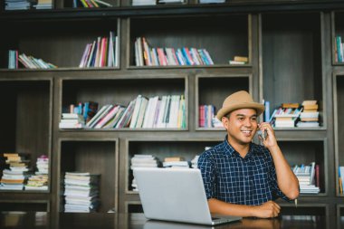 Genç hippi Asyalı işadamı akıllı telefon ve dizüstü bilgisayarını Planlama projeleri için kullanıyor.