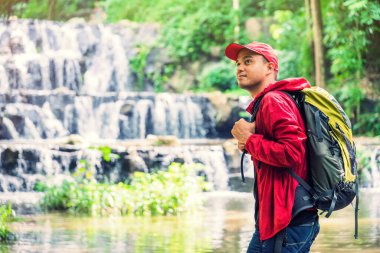 Şelalenin yanındaki sonbahar ormanında yürüyüş yapan mutlu sırt çantalı adam. Tra