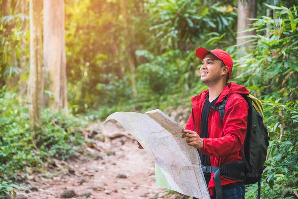 Asian traveller man searching right direction on map in the forest with copy space.