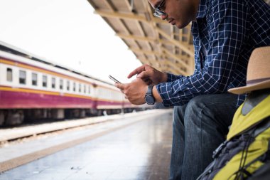 Treni beklerken akıllı telefonu tutan genç bir gezgin.