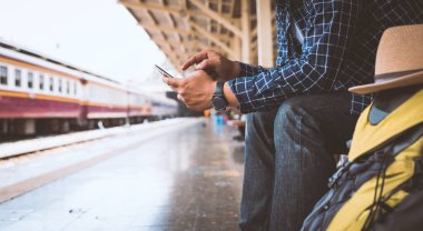 Treni beklerken akıllı telefonu tutan genç bir gezgin.