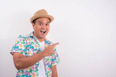 Şok olmuş genç adam boş bir yeri işaret ediyor. Yazlık gömlek giyiyor..