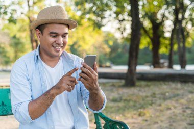 Genç Asyalı adam parkta akıllı telefon kullanıyor.