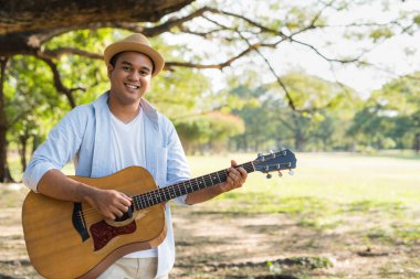 Genç Asyalı adam parkta gitar çalıyor.