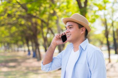 Genç Asyalı adam parkta akıllı telefon kullanıyor.